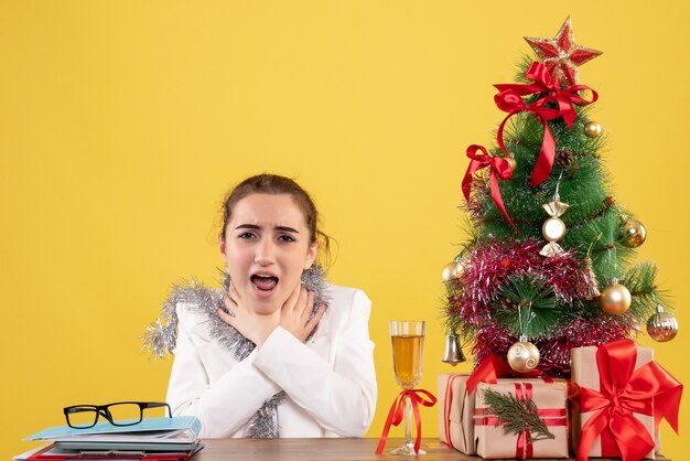 Médica de frente, sentada atrás da mesa, com problemas de respiração, em fundo amarelo, cor do feriado, Natal, ano novo, emoção, enfermeira