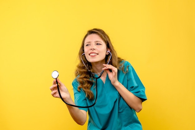 Médica de frente usando estetoscópio no espaço amarelo