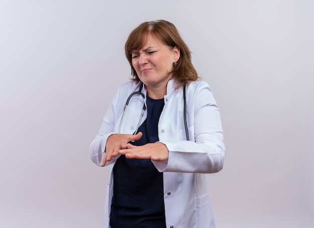 Médica de meia-idade descontente, vestindo túnica médica e estetoscópio, levantando as mãos em um fundo branco isolado com espaço de cópia