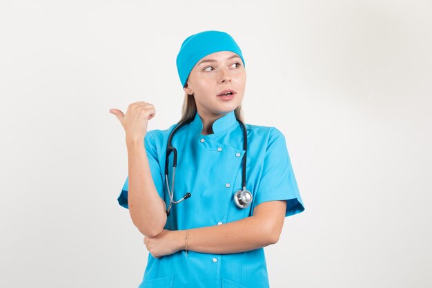 Médica de uniforme azul apontando para trás com o polegar