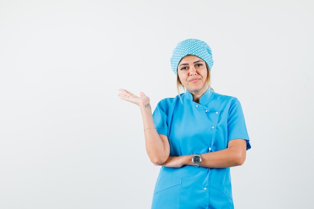 Médica de uniforme azul com a palma da mão levantada e parecendo confusa