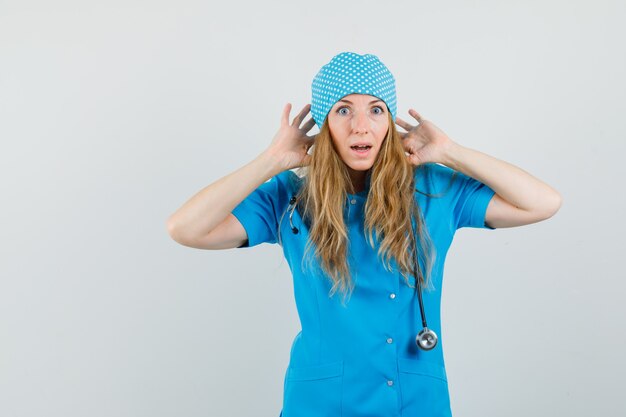 Médica de uniforme azul com as mãos perto das orelhas e parecendo ansiosa