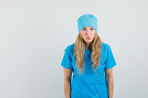 Médica de uniforme azul com os lábios dobrados e com uma aparência engraçada
