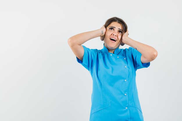 Médica de uniforme azul de mãos dadas nas orelhas e surpresa