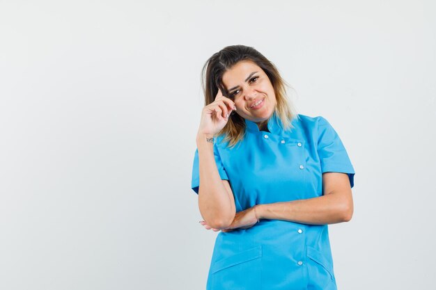 Médica de uniforme azul em pose pensativa e parecendo alegre