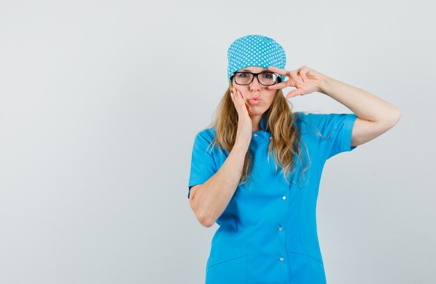 Médica de uniforme azul mostrando o sinal V perto do olho e fazendo beicinho nos lábios