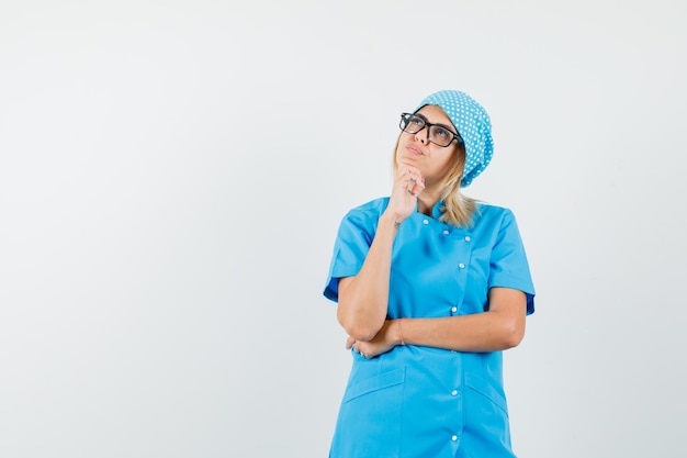 Médica de uniforme azul olhando para cima e parecendo pensativa