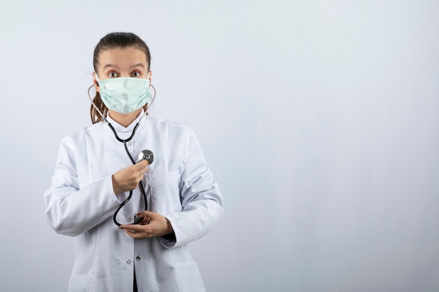 Foto grátis médica de uniforme branco usando uma máscara médica e segurando um estetoscópio