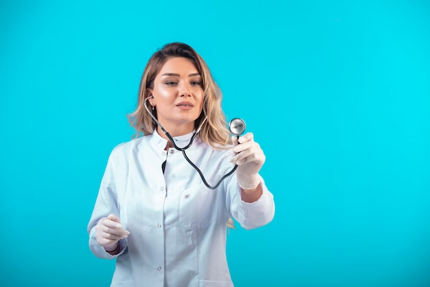 Médica de uniforme branco, verificando com estetoscópio e ouvindo com atenção.