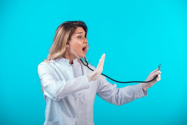 Médica de uniforme branco, verificando com estetoscópio.