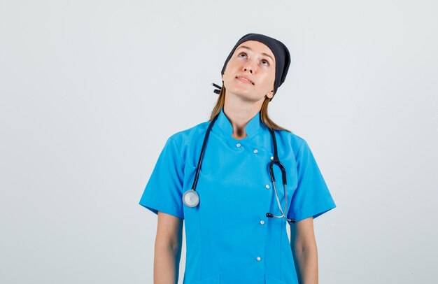 Médica de uniforme olhando para cima e parecendo esperançosa