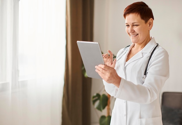 Médica do centro de recuperação cobiçoso, sorridente, idosa, com tablet e estetoscópio