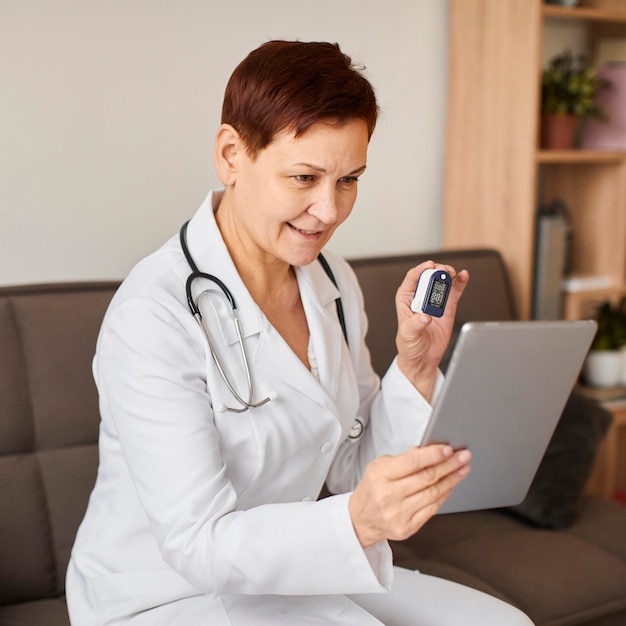 Médica do centro de recuperação cobiçoso, sorridente, idosa, com tablet e oxímetro