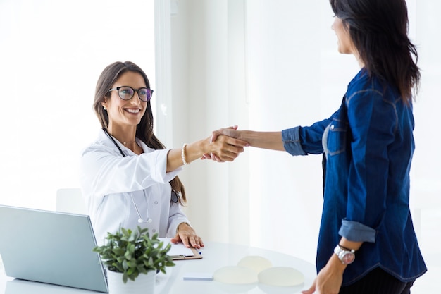 Médica do sexo feminino e seu paciente apertando as mãos na consulta.