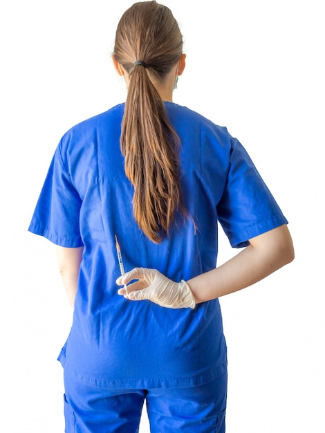 Médica em um uniforme médico azul com luvas esterilizadas, segurando uma seringa nas costas