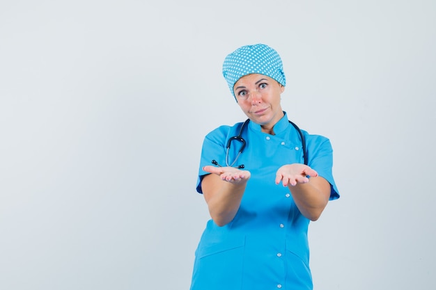 Médica em uniforme azul, oferecendo algo e parecendo vista frontal suave.