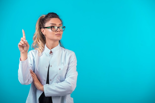 Médica em uniforme branco, pedindo atenção.