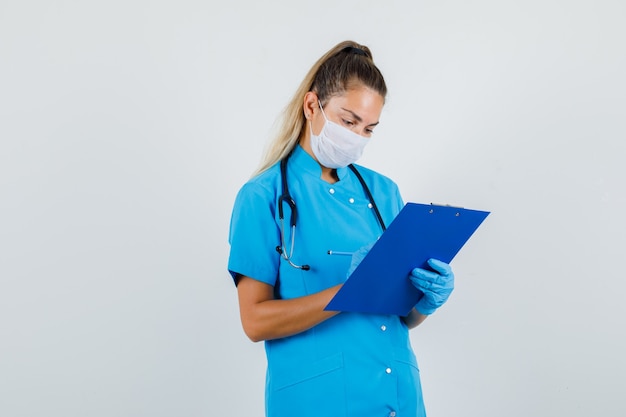 Médica fazendo anotações na prancheta com uniforme azul