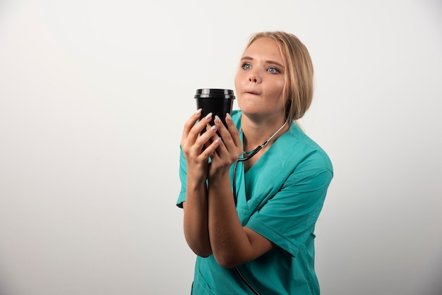 Médica loira posando com uma xícara de café.
