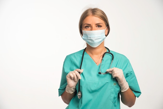 Médica loira usando máscara e colocando um estetoscópio no pescoço