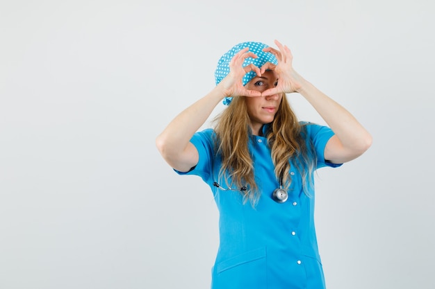 Médica mostrando gesto de coração em uniforme azul e parecendo alegre