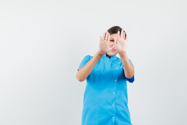 Médica mostrando gesto de recusa em uniforme azul e parecendo envergonhada