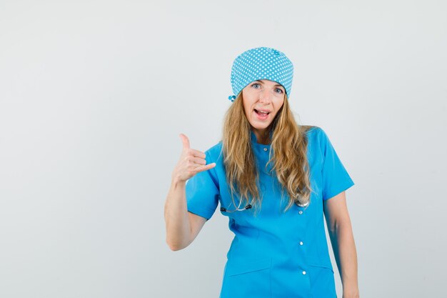 Médica mostrando gesto de telefone com uniforme azul e parecendo confiante