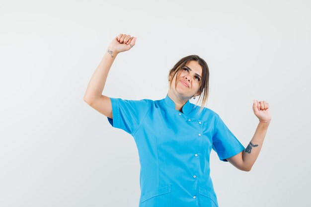 Médica mostrando gesto de vencedor em uniforme azul e parecendo feliz