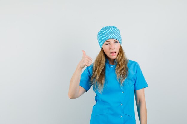 Médica mostrando o polegar e o olho piscando em uniforme azul