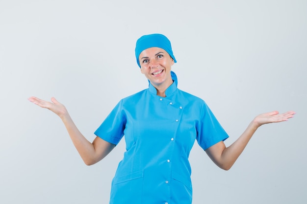 Médica mostrando ou comparando algo em uniforme azul e parecendo alegre. vista frontal.