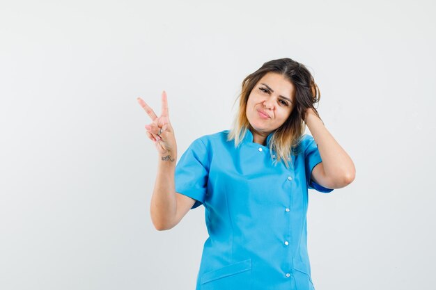 Médica mostrando sinal de vitória com uniforme azul e aparentando estar compartilhando