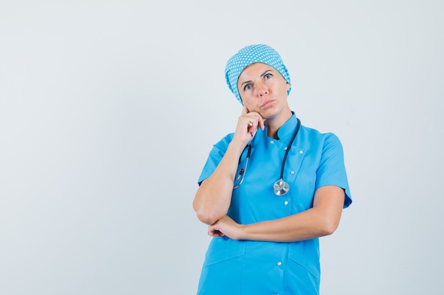 Médica olhando em uniforme azul e olhando pensativa. vista frontal.
