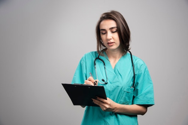 Médica olhando para a área de transferência em fundo cinza. Foto de alta qualidade