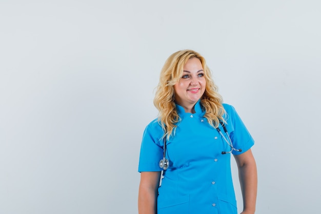 Médica olhando para o lado com uniforme azul e feliz com o espaço para texto