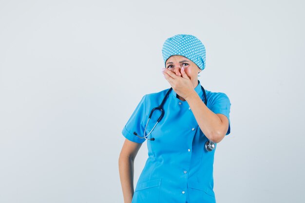 Médica, segurando a mão na boca em uniforme azul e parecendo feliz. vista frontal.