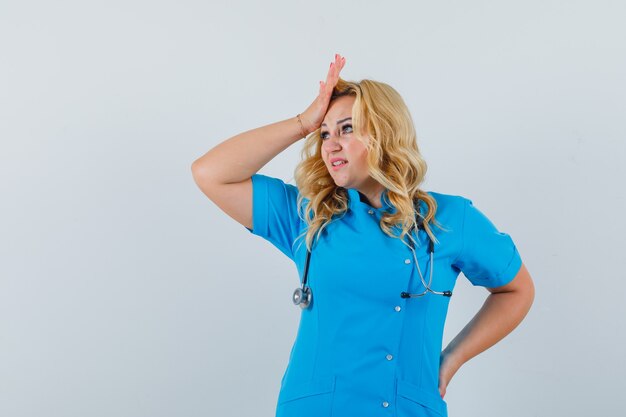 Médica segurando a mão na testa com um uniforme azul e parecendo preocupada