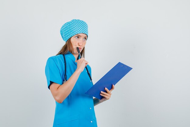 Médica segurando a prancheta e uma caneta com uniforme azul e parecendo ocupada. vista frontal.