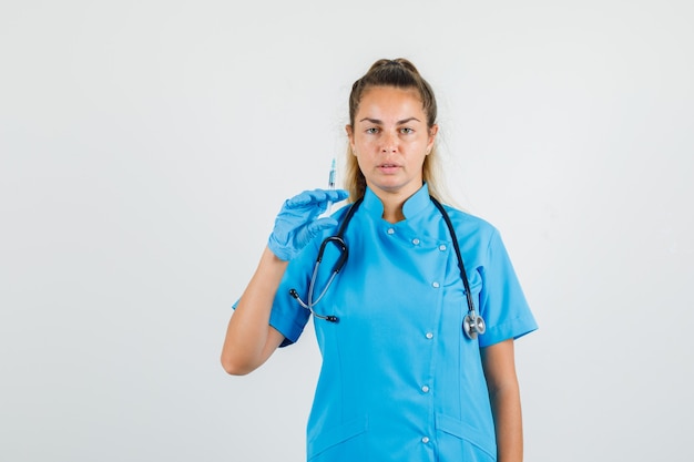 Médica segurando seringa para injeção em uniforme azul, luvas