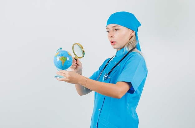 Médica segurando uma lupa sobre o globo em um uniforme azul e parecendo surpresa