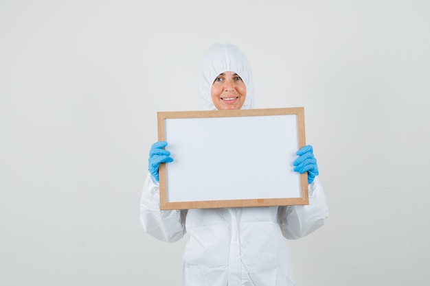 Médica segurando uma moldura em branco em um traje de proteção