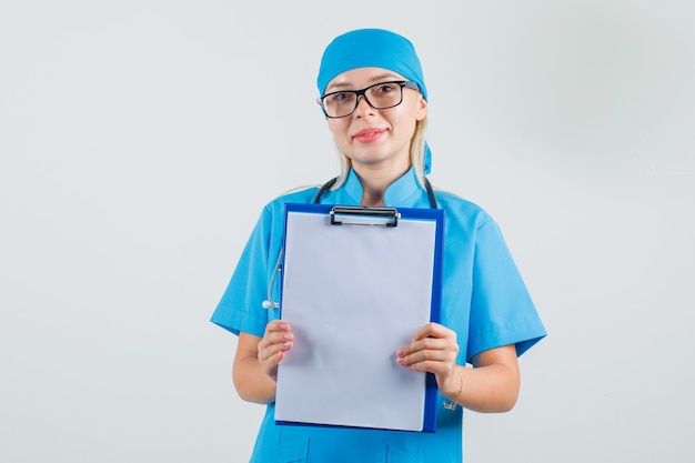 Médica segurando uma prancheta com uniforme azul, óculos e parecendo alegre