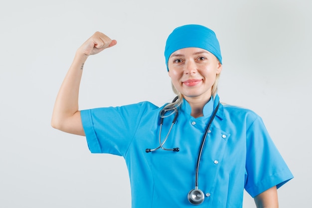 Médica sorrindo e mostrando músculos em uniforme azul e parecendo confiante
