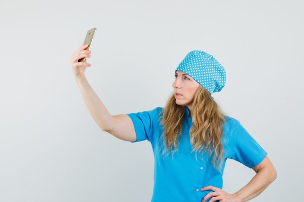 Médica tirando selfie no celular com uniforme azul