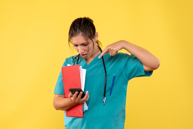 Médica vista frontal com camisa médica segurando a análise e o telefone no fundo amarelo