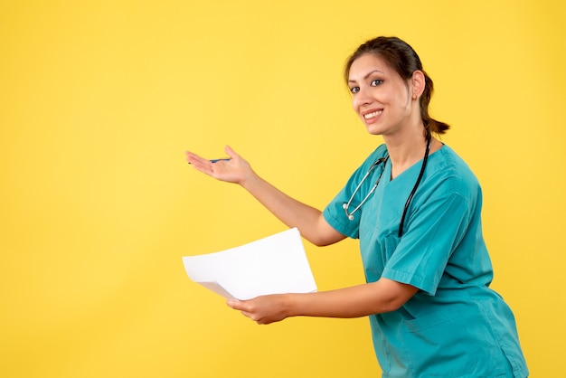 Médica vista frontal com camisa médica segurando análise de papel sobre fundo amarelo