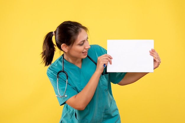 Médica vista frontal com camisa médica segurando análise de papel sobre fundo amarelo