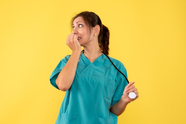 Médica vista frontal com camisa médica, sentindo-se nervosa em fundo amarelo