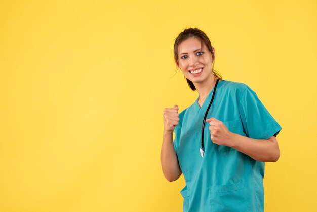 Médica vista frontal com camisa médica sorrindo sobre fundo amarelo