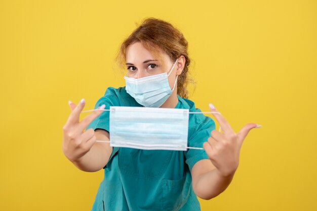 Médica vista frontal com máscara de camisa médica e segurando outra máscara, cor covid-19 vírus saúde emoção pandemia