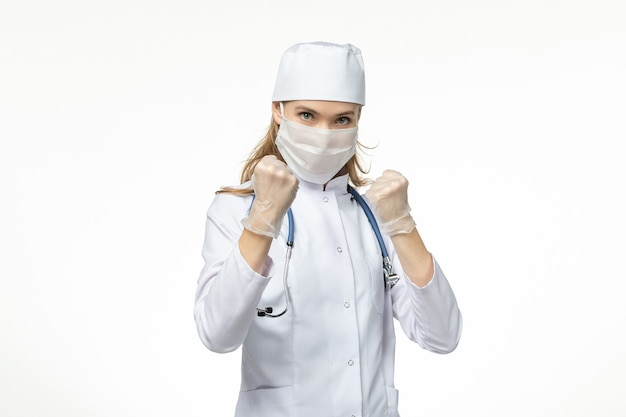 Médica vista frontal com traje médico com máscara e luvas devido ao coronavírus na luta contra a doença da parede branca-clara vírus covidêmico